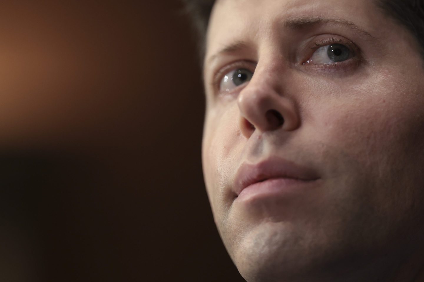 A very close-up photo of Sam Altman's pensive face.