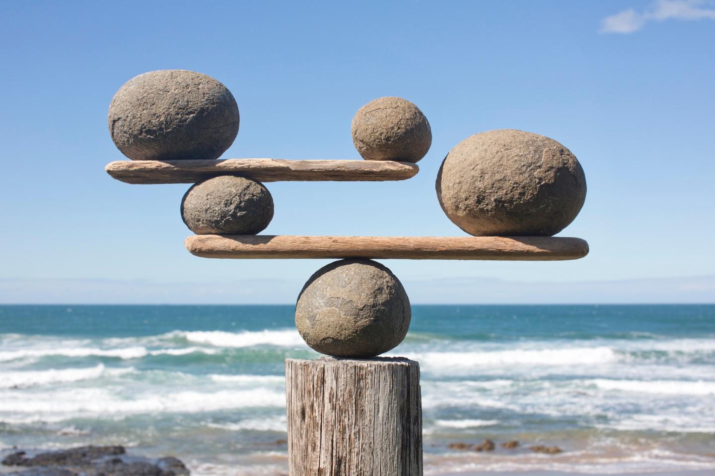 Photo: Rocks balancing on driftwood, sea in background.