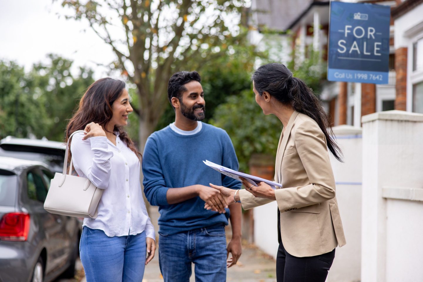 Indian couple greeting a real estate agent in the street for a house showing and smiling.