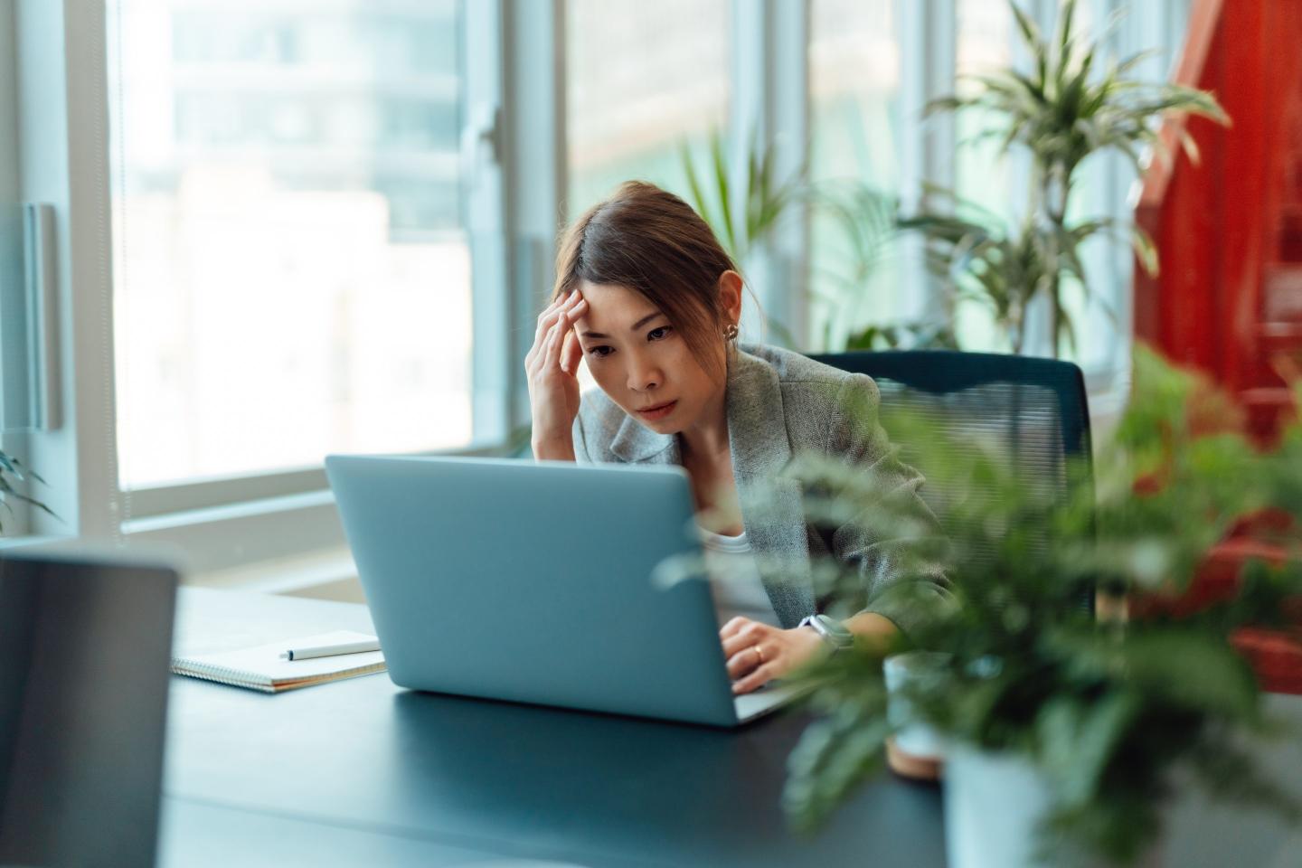 A worried businesswoman looks at a laptop computer in an office.
