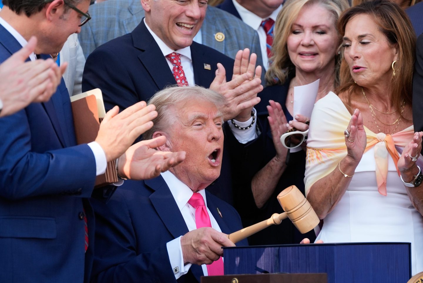 Donald Trump sits and bangs a gavel as people around him applaud.