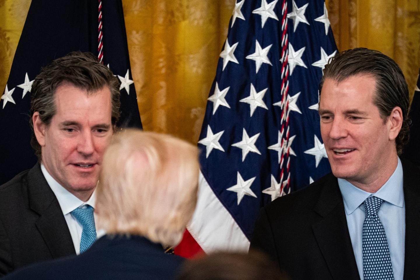Cameron Winklevoss, co-founder and president of Gemini Trust Co., left, and Tyler Winklevoss, co-founder and chief executive officer of Gemini Trust Co., right, speak with US President Donald Trump during a signing ceremony for the GENIUS Act in the East Room of the White House in Washington, DC, US, on Friday, July 18, 2025.