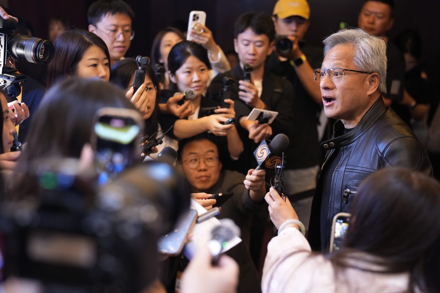 Tech CEO surrounded by throng of reporters holding phones and recorders in front of him.