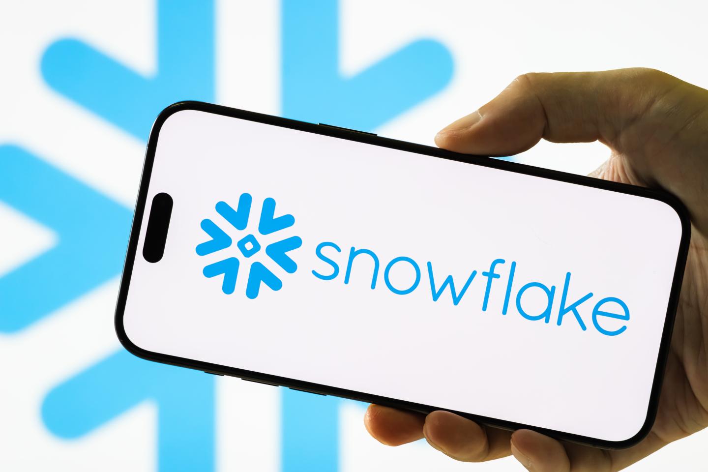 In this photo illustration, a hand holds a smartphone displaying the logo of Snowflake Inc. (NYSE: SNOW), an American cloud-based data warehousing company, with the company.