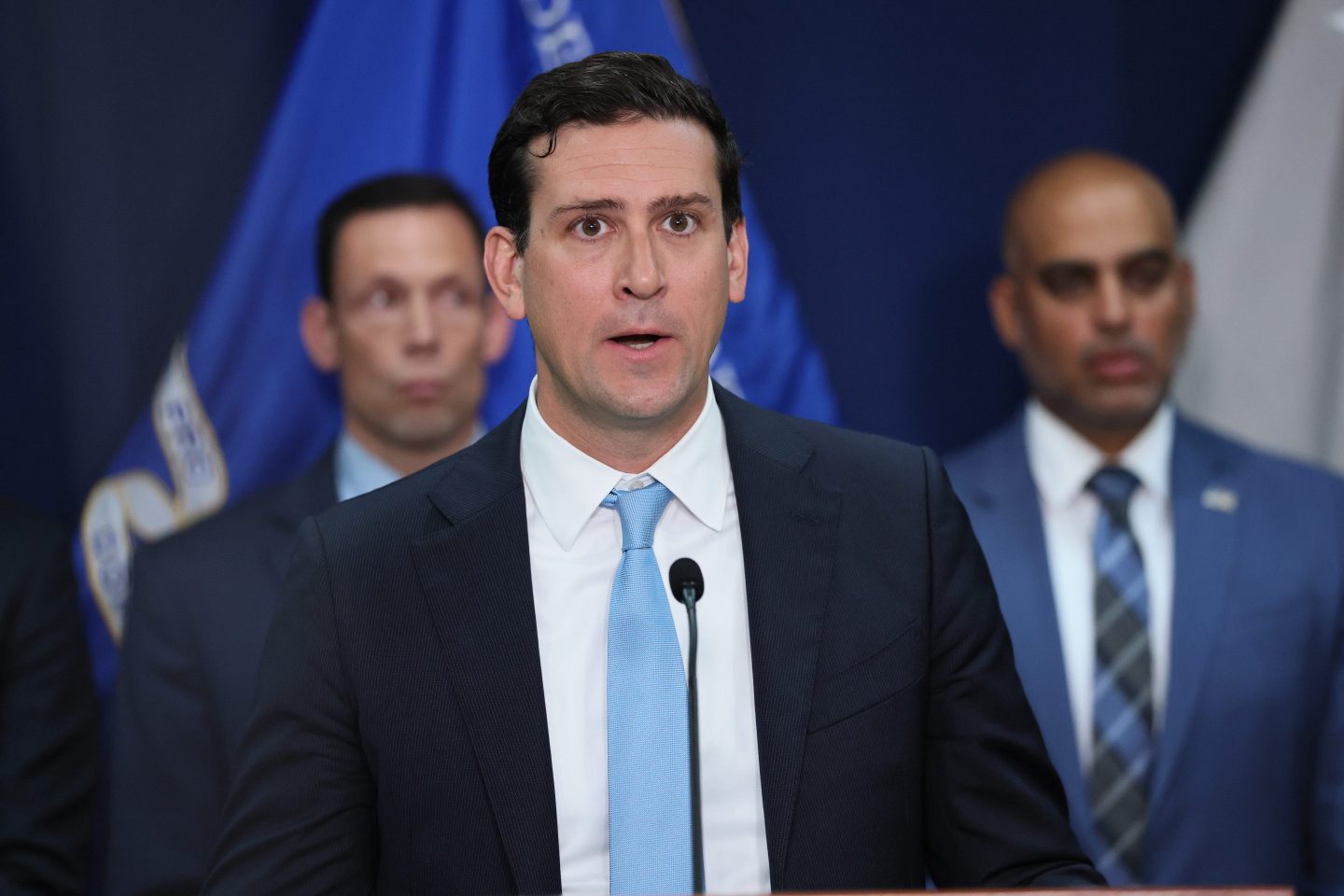 Man with dark hair and a dark suit and light blue tie.