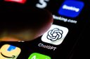 Someone's index finger poised over the ChatGPT app icon on the touchscreen of a smartphone.