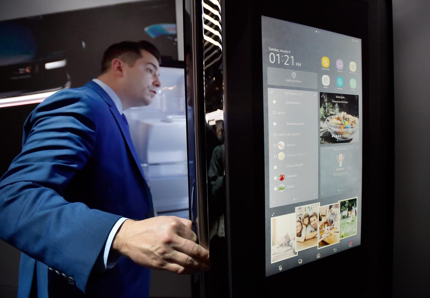 A man opens up a refrigerator door, which has a display screen on it.