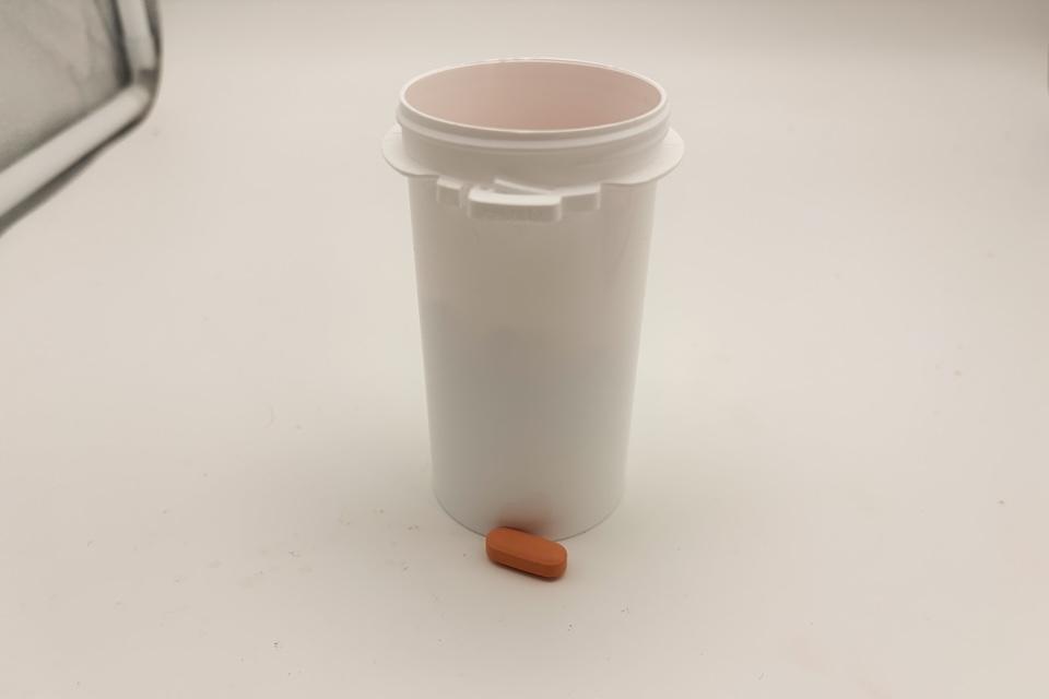 A white bottle of Wisp Prenatal Vitamins, with one of the capsules sitting next to it.