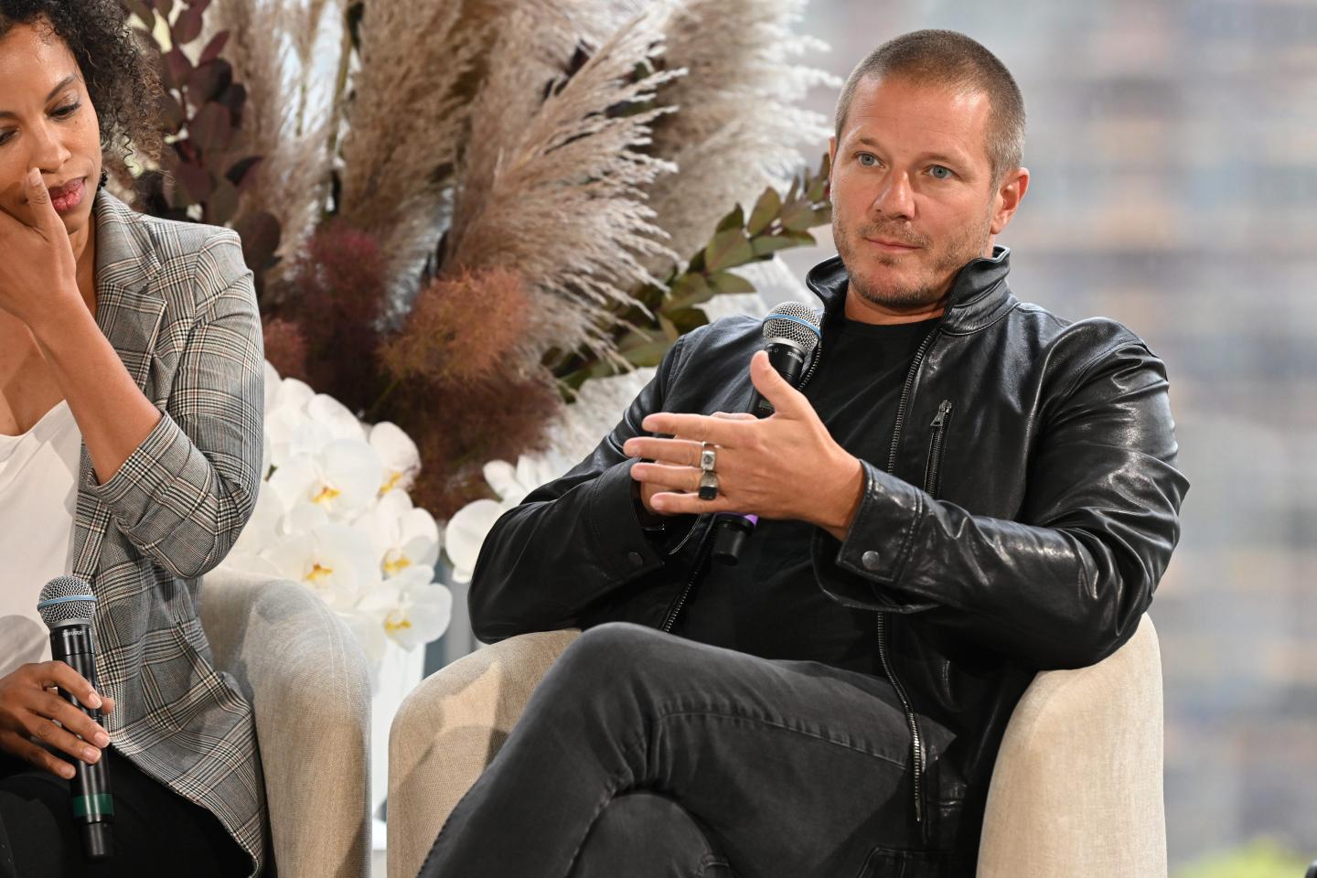 Shawn Nelson sits in a white chair in an all-black outfit, gesturing with his left hand.