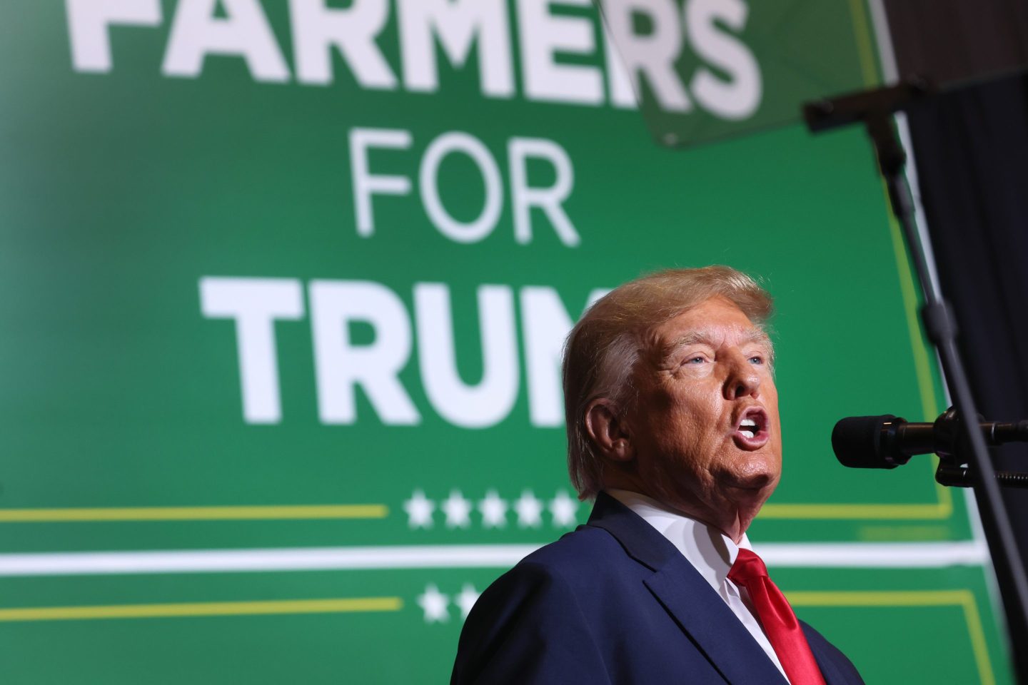 Donald Trump speaks in front of a green "Farmers for Trump" background.