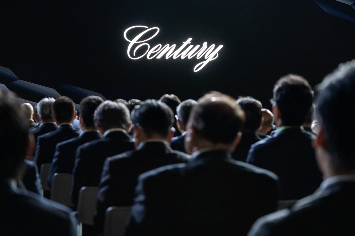 Men sit in chairs looking at the Toyota Century logo