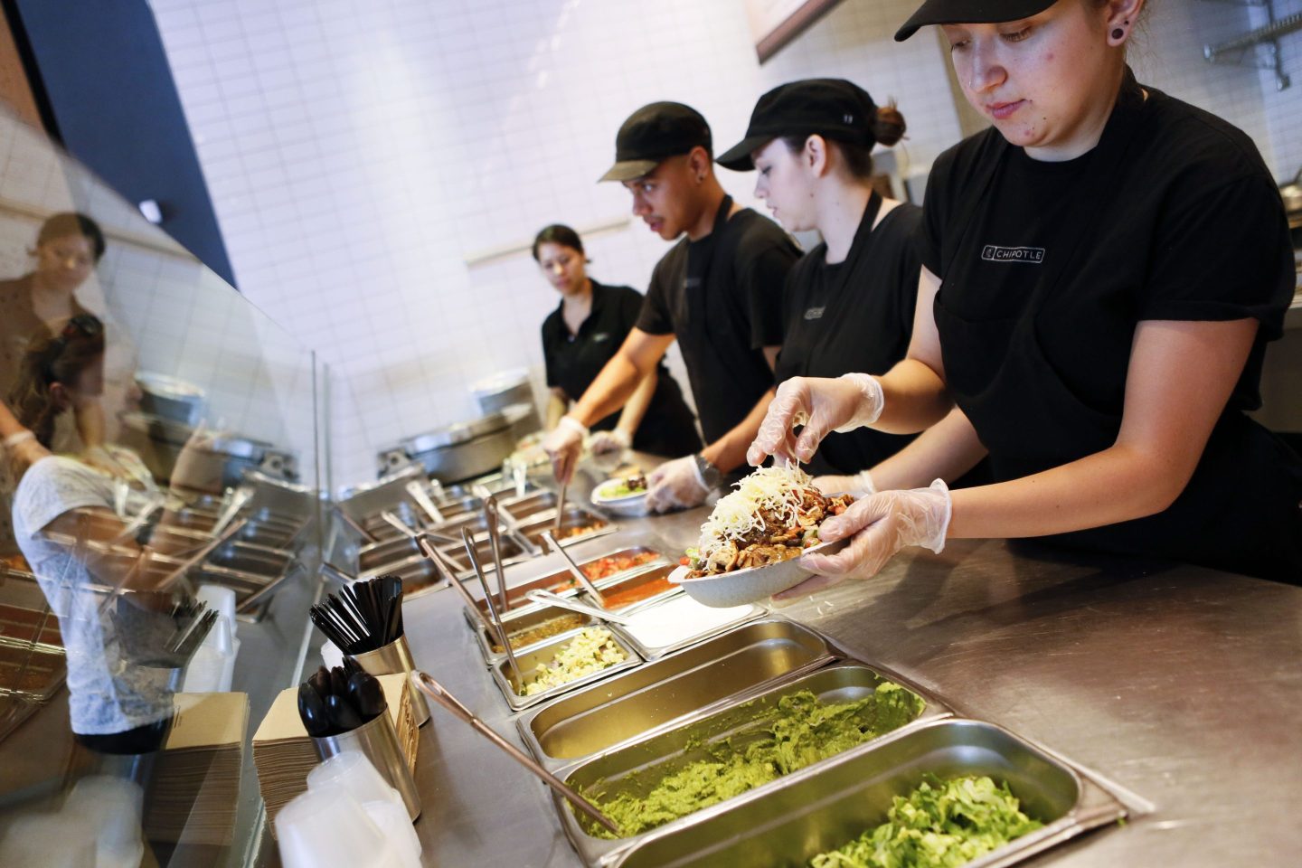 A line of Chipotle workers behind the counter assemble burrito bowls.