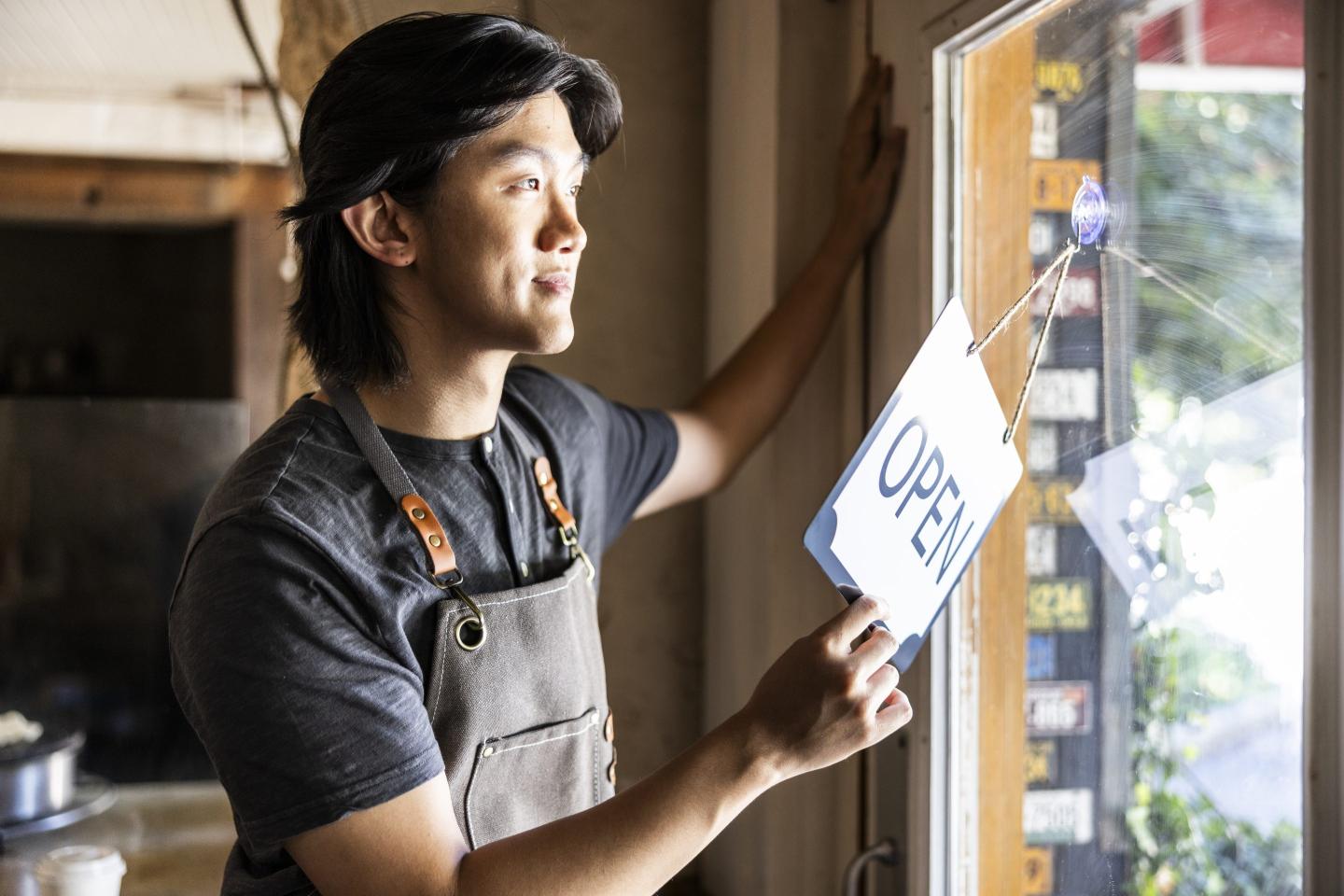 Small business owner placing open sign in business window