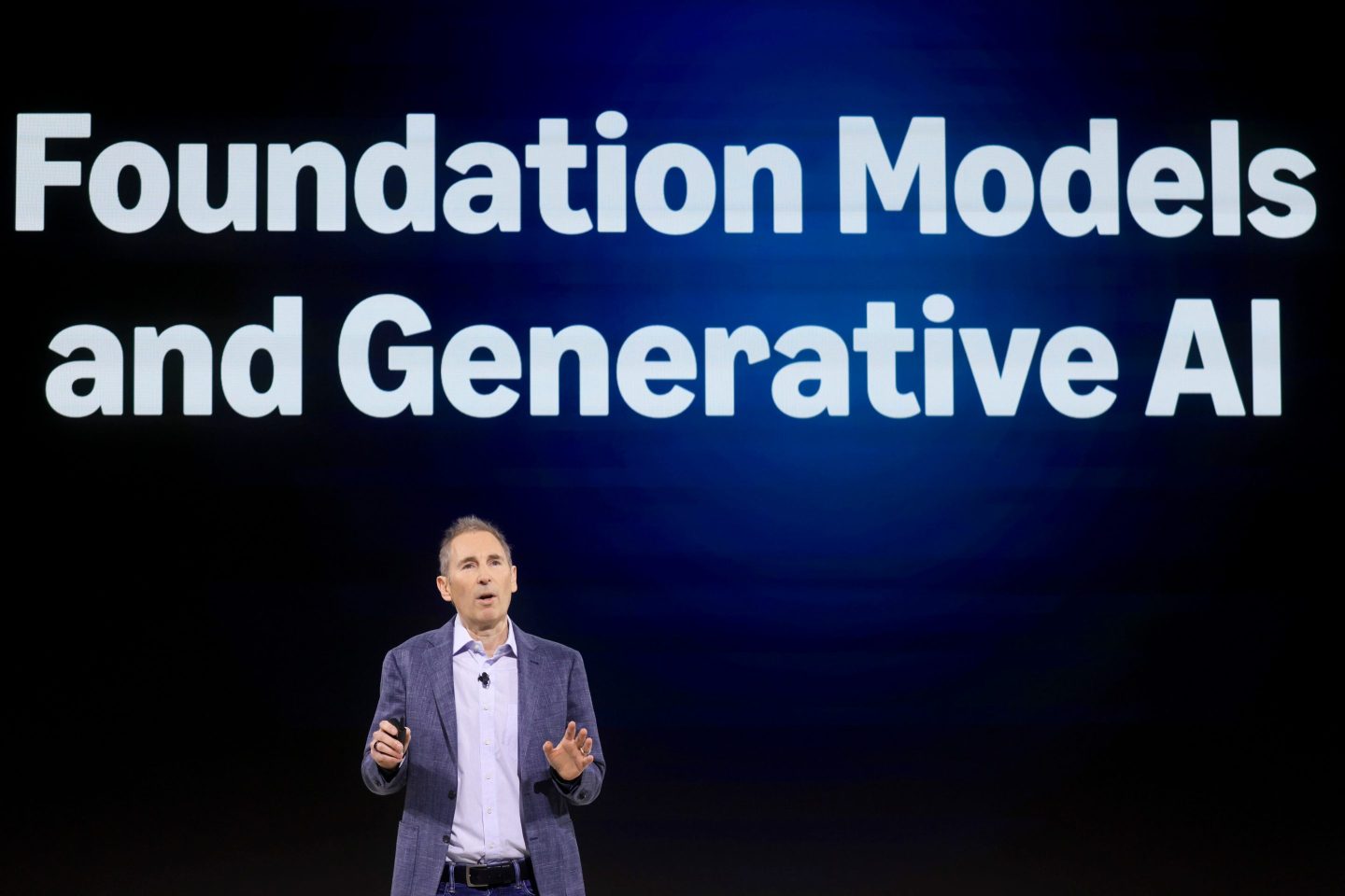 A man stands on stage under a visual about AI models