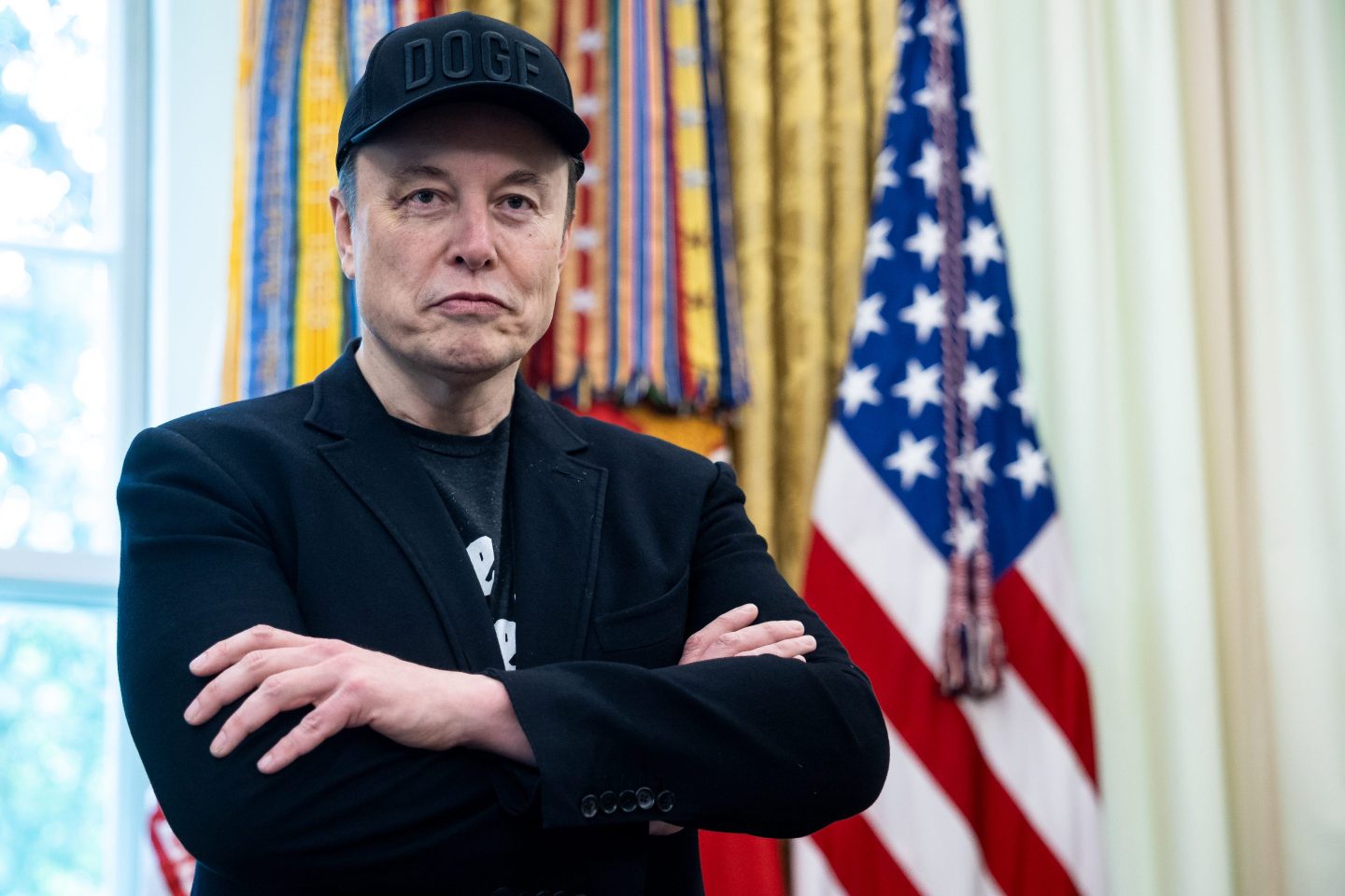 Elon Musk in the Oval Office with his arms crossed