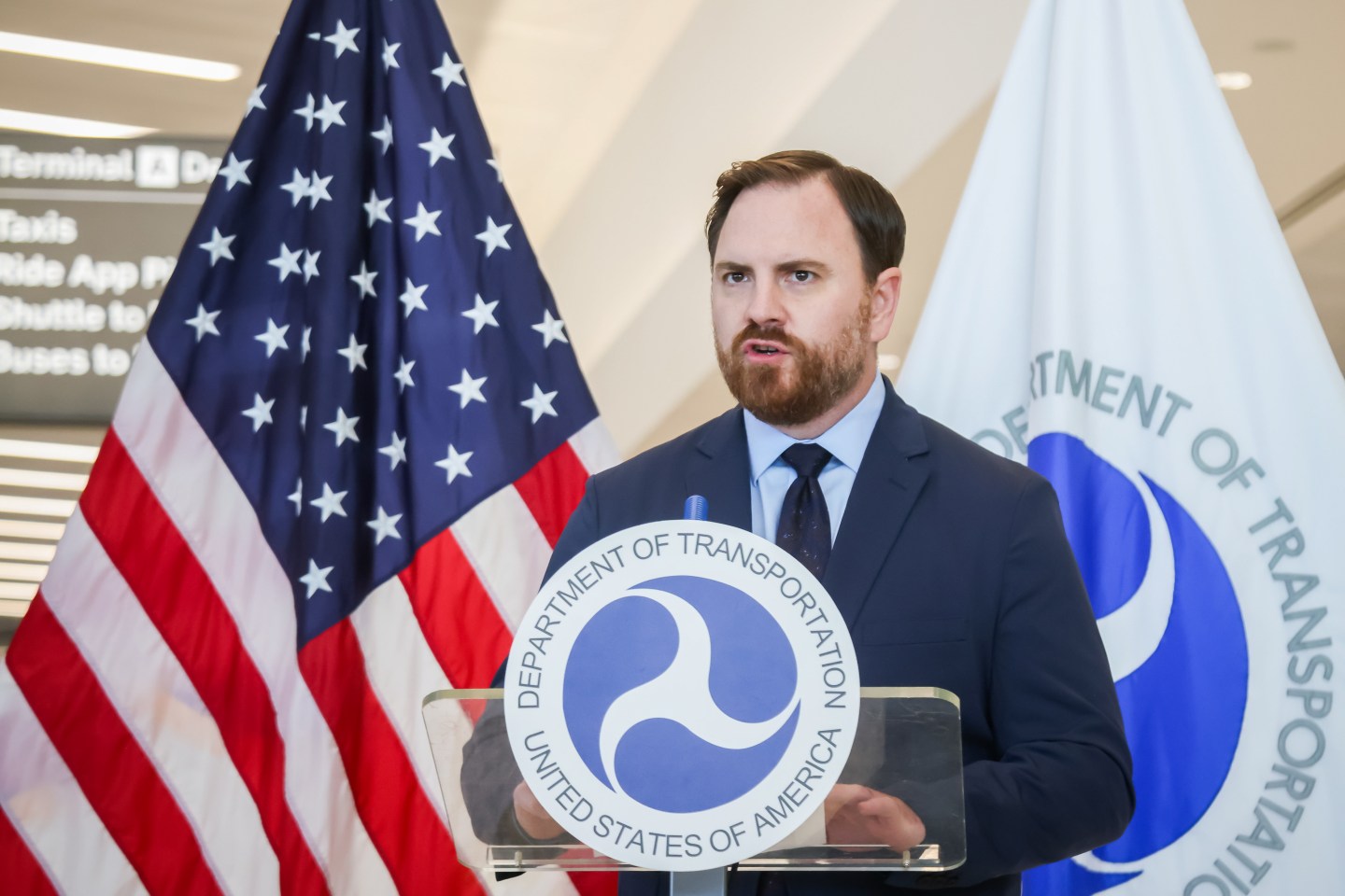 Nick Daniels speaks in front of an America flag and behind a podium with the Department of Transportation logo on it.