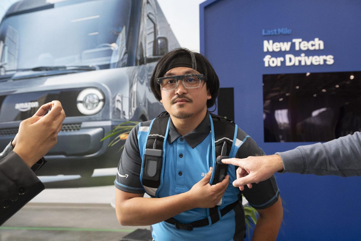 An Amazon delivery driver wears a pair of dark glasses and touches the side of a vest he is wearing.