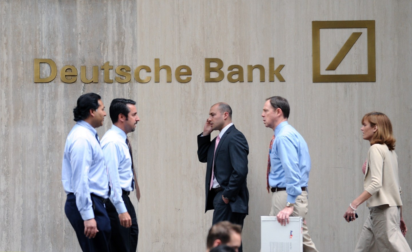 pedestrians walk in front of Deutsche Bank sign