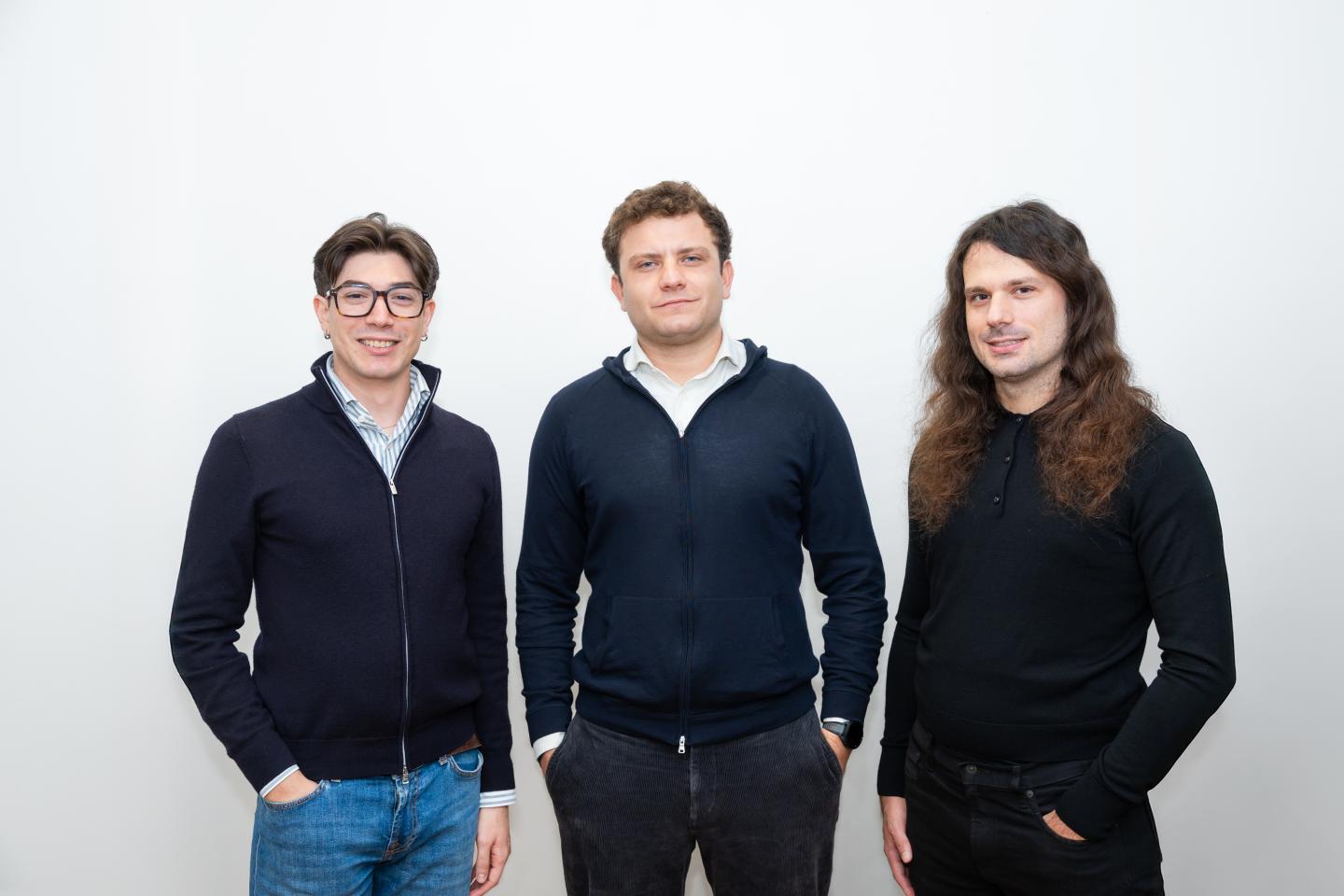 Three men stand in front a white backdrop.
