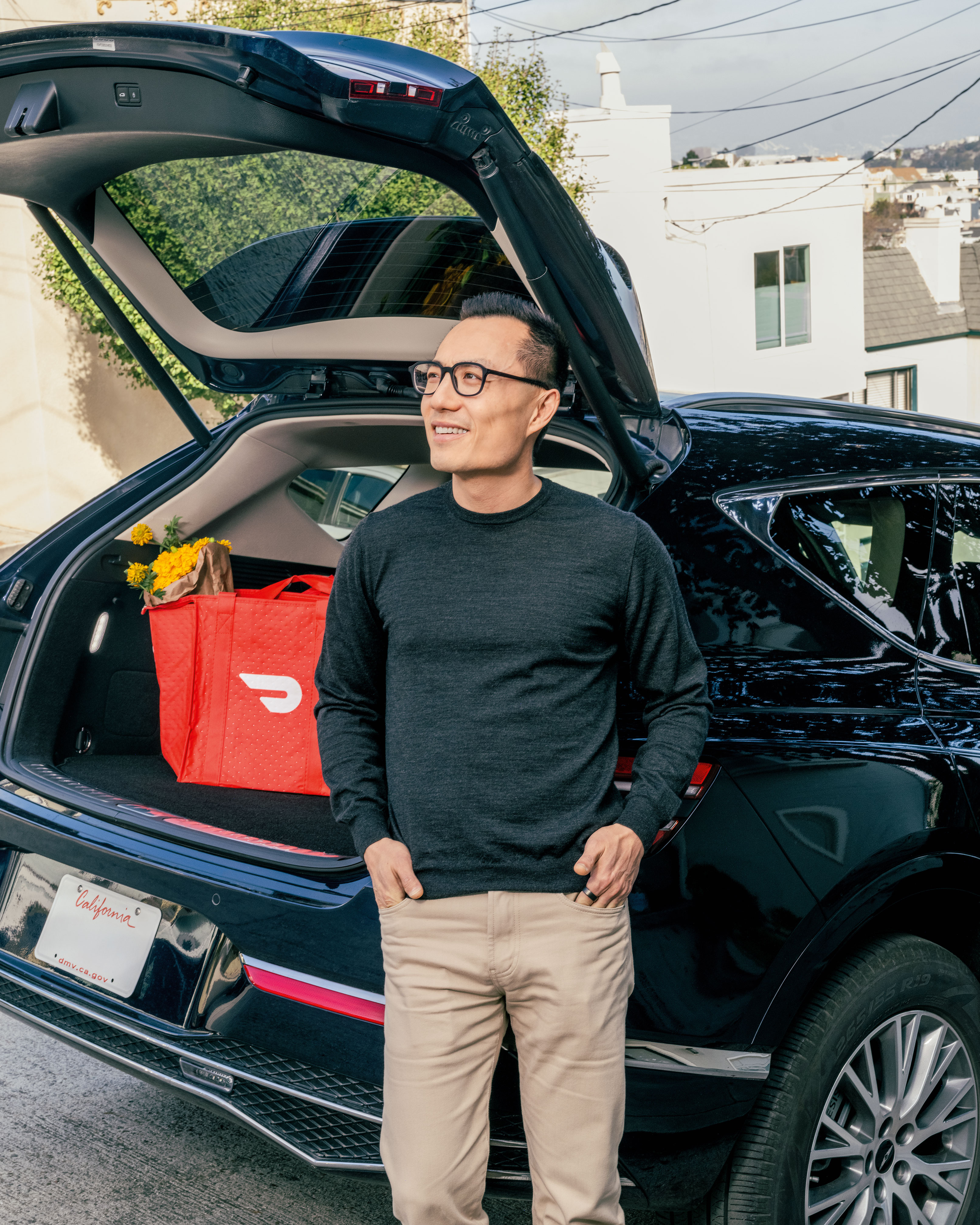 A man stands in front of the trunk of a car with a DoorDash bag in the trunk.