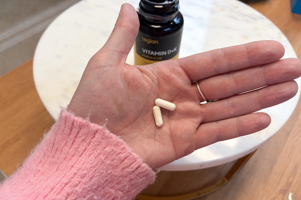 Clear Legion Vitamin D+K capsules in a woman's hand.