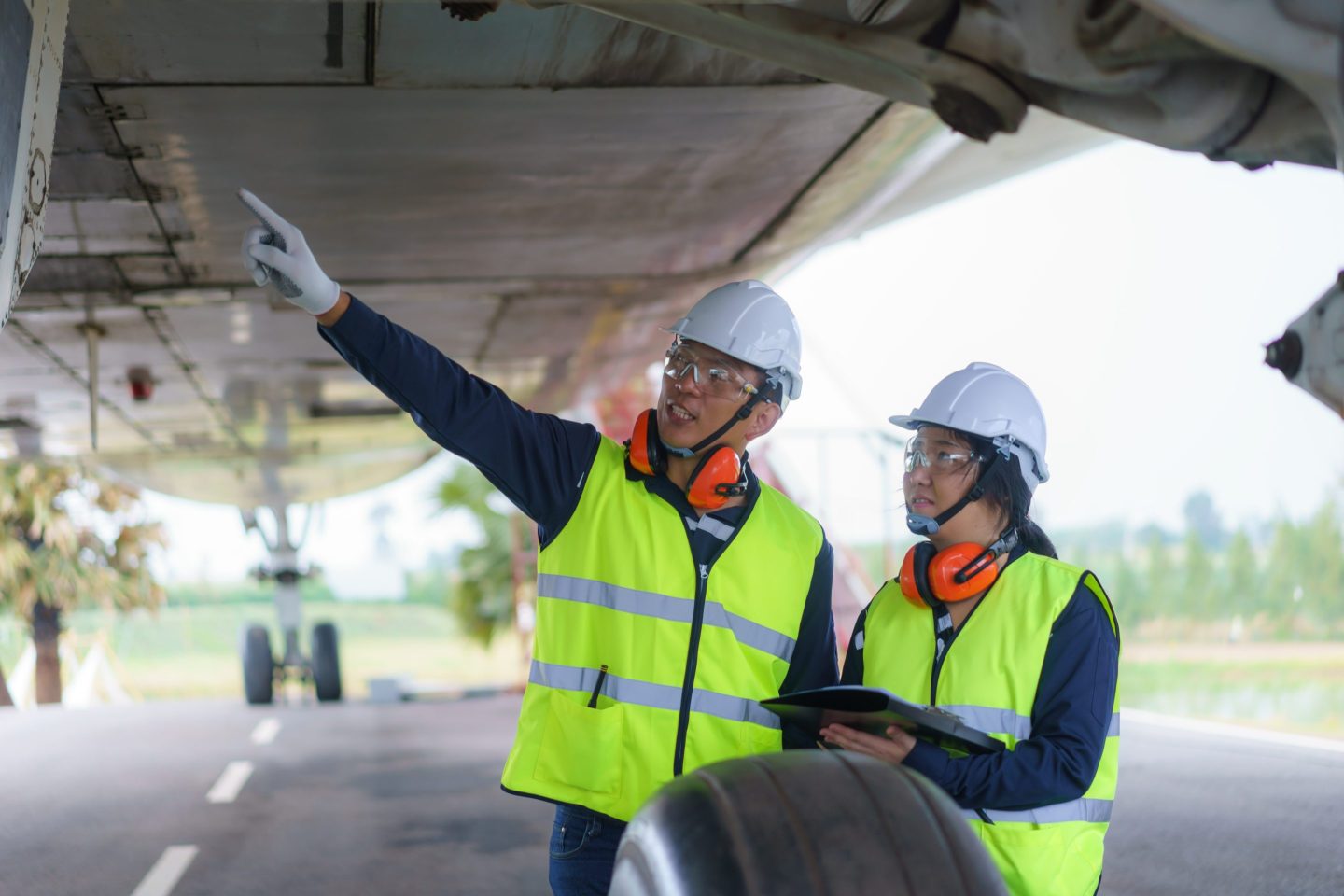 Engineers wear helmets and high-visitability vests while inspecting an aircraft