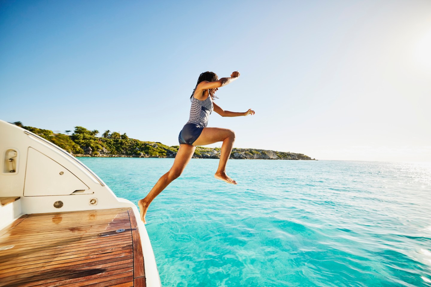 Wide shot of teenage girl jumping off swim step of yacht into Caribbean Sea during family vacation