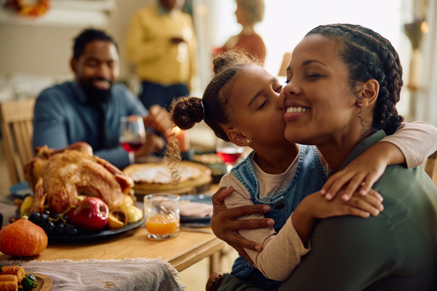 Daughter kisses mom at Thanksgiving table.