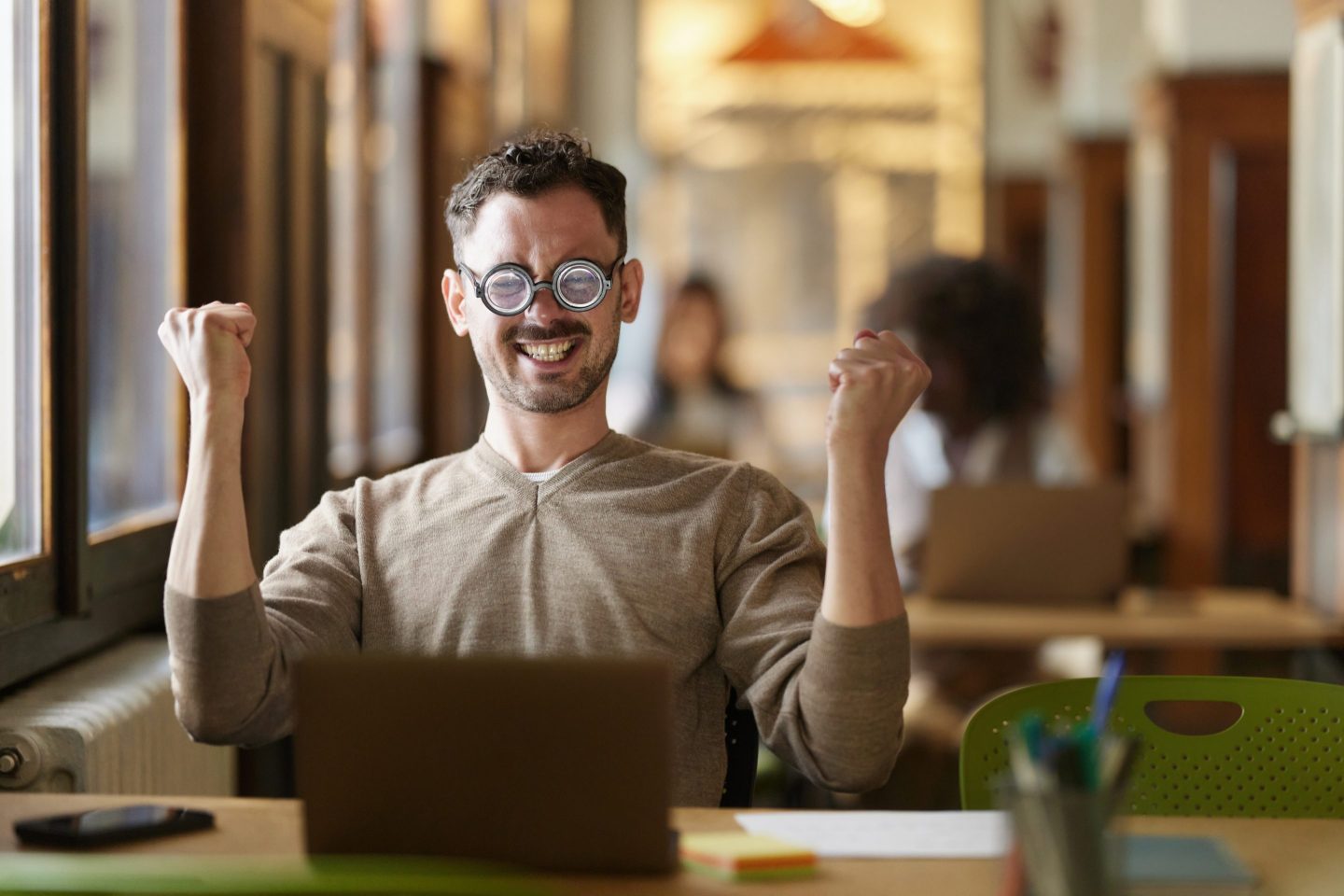 Nerdy male freelancer celebrating his achievement while working on a computer in the office.
