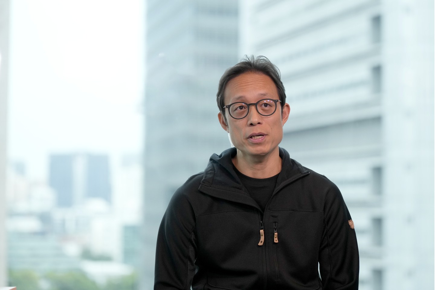 A man in a black hoodie and glasses is speaking