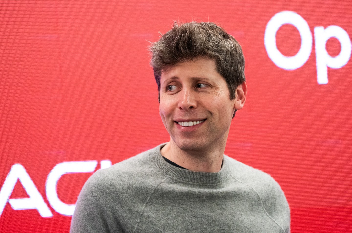 Sam Altman smiles against a pink background