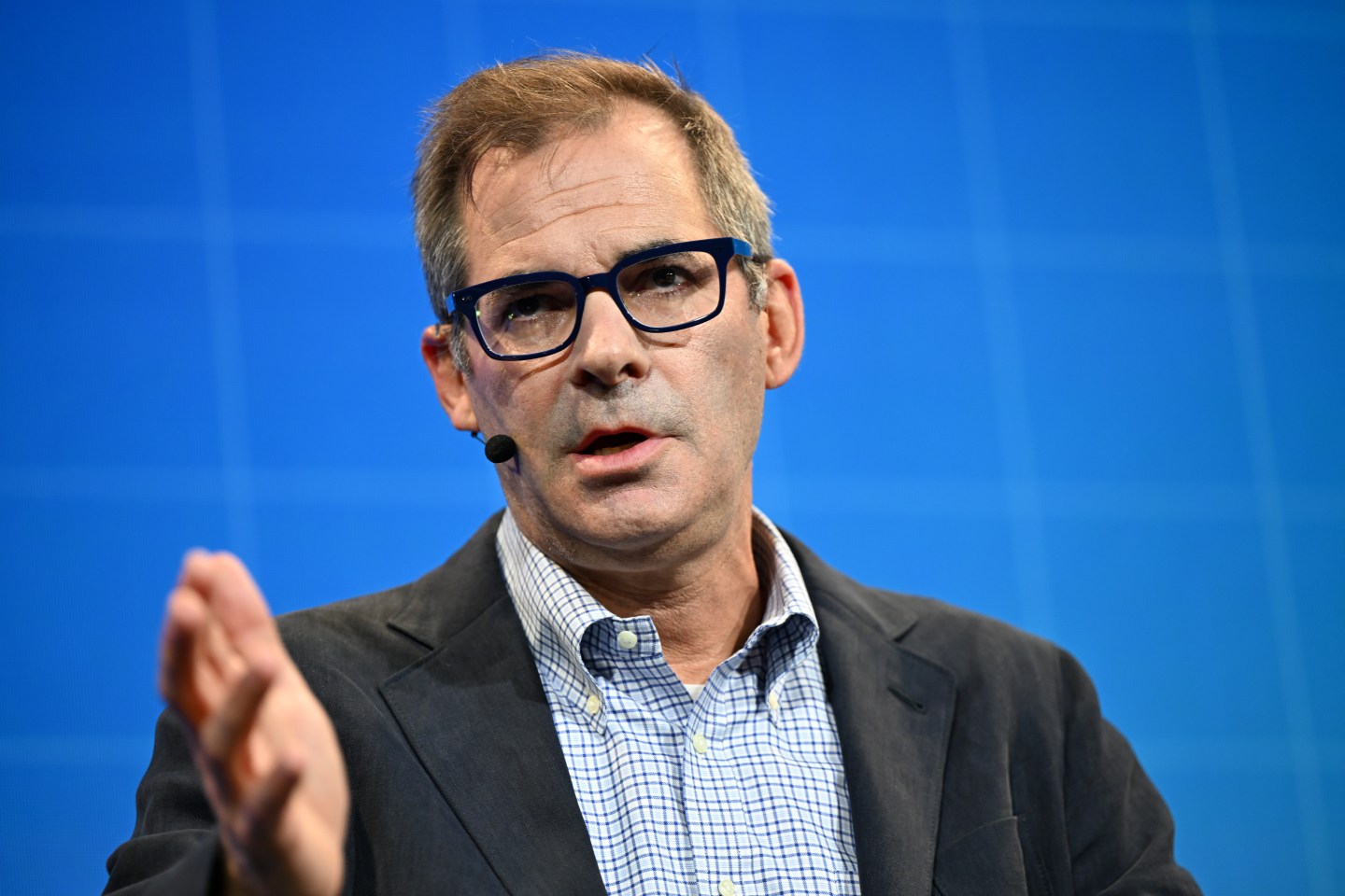 Man gesturing with a suit coat and blue shirt and blue background
