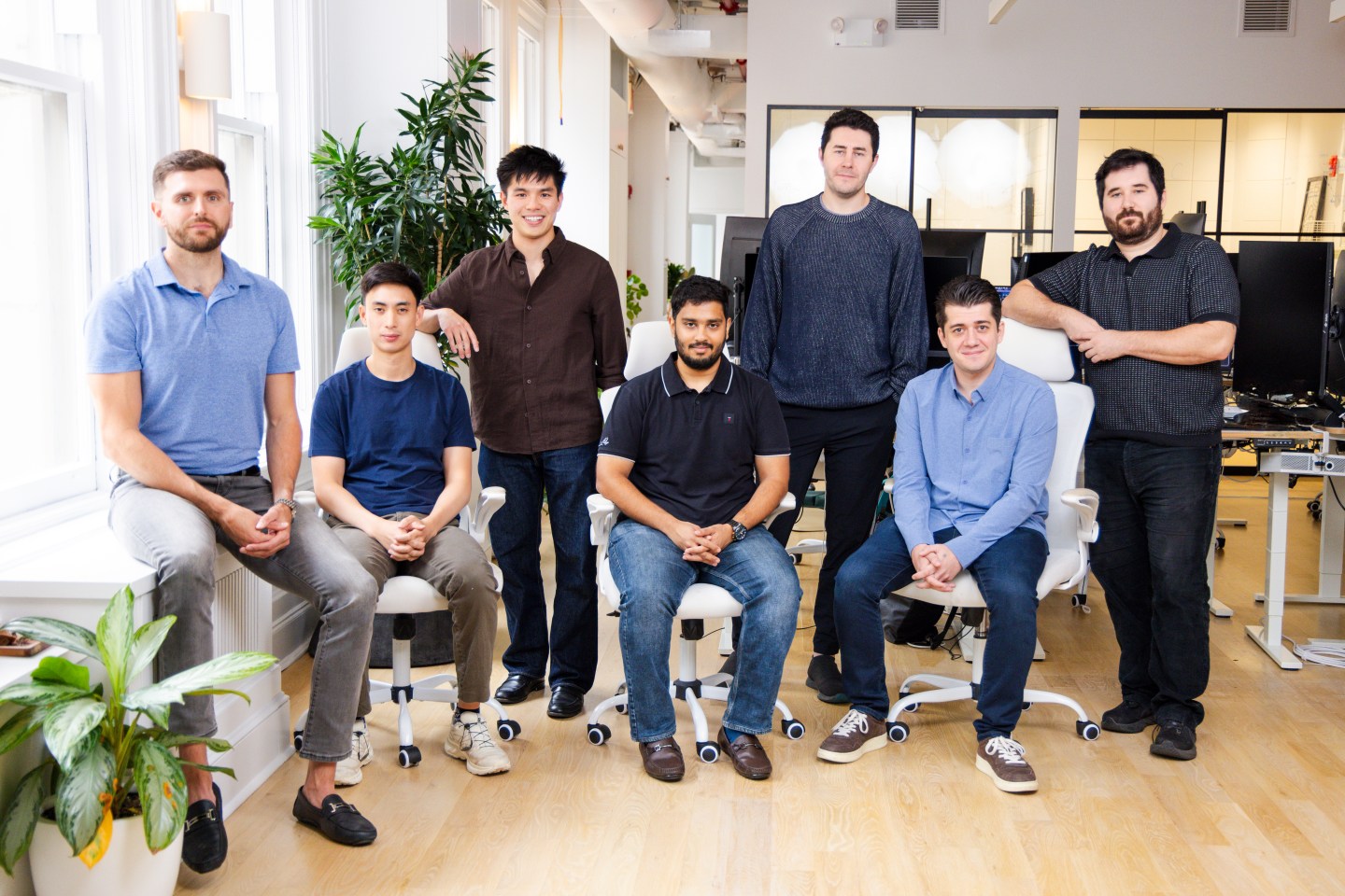 Seven men stand and sit in a modern-looking office