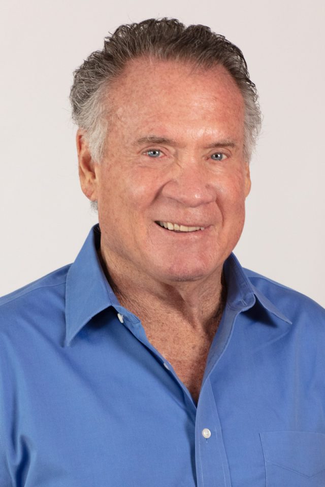 Neil Kiefer is wearing a blue shirt and smiling while looking at the camera