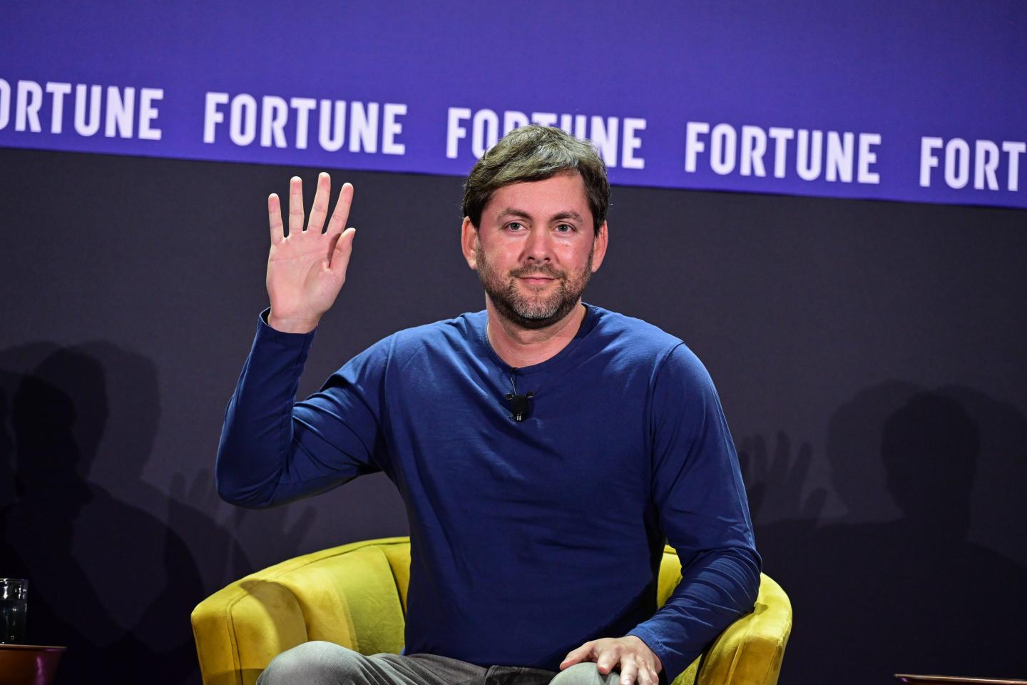 Jesse Levinson sits in a yellow chair in front of a purple "Fortune" background. He is waving with his right hand.