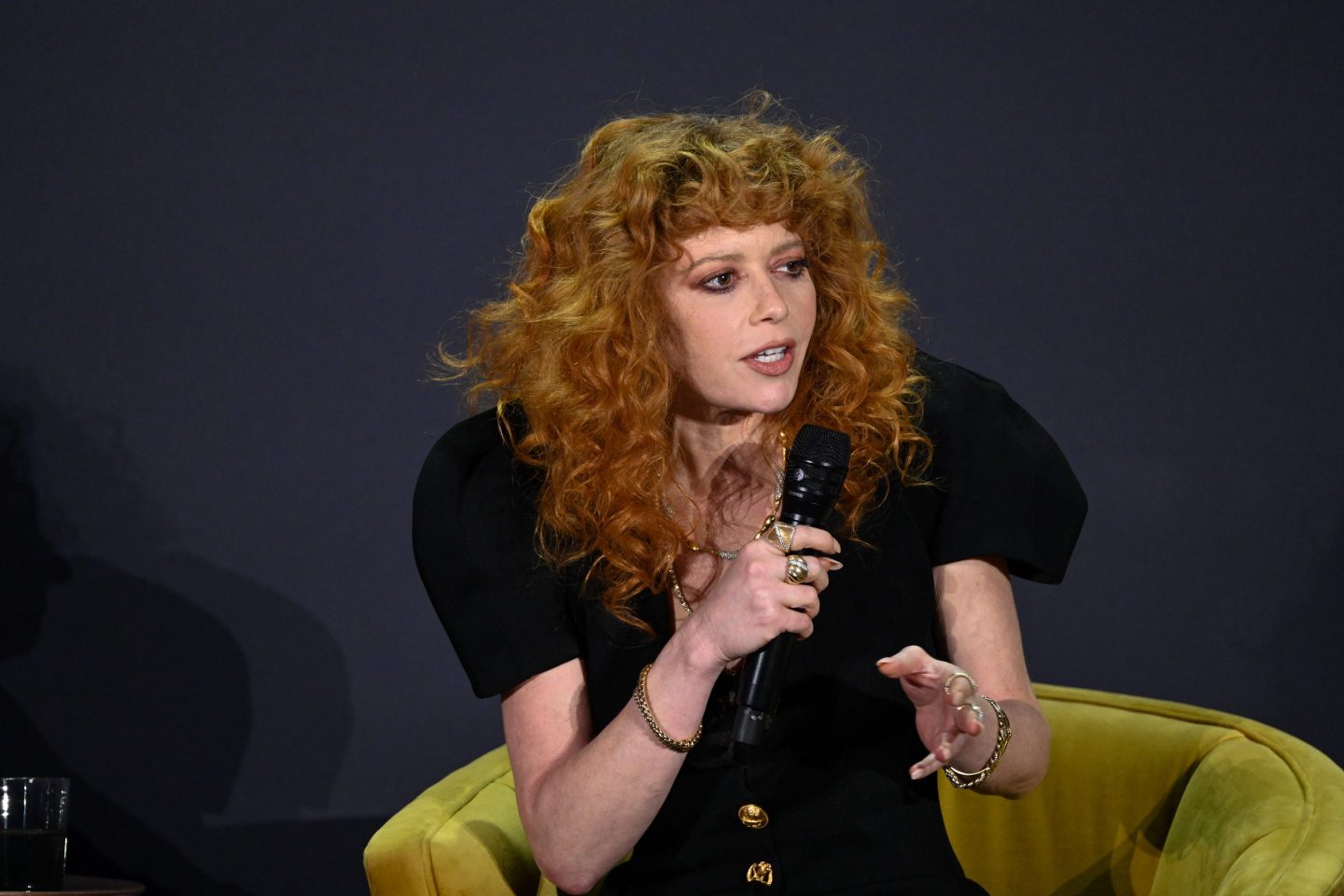 Curly haired woman in a black dress speaking.