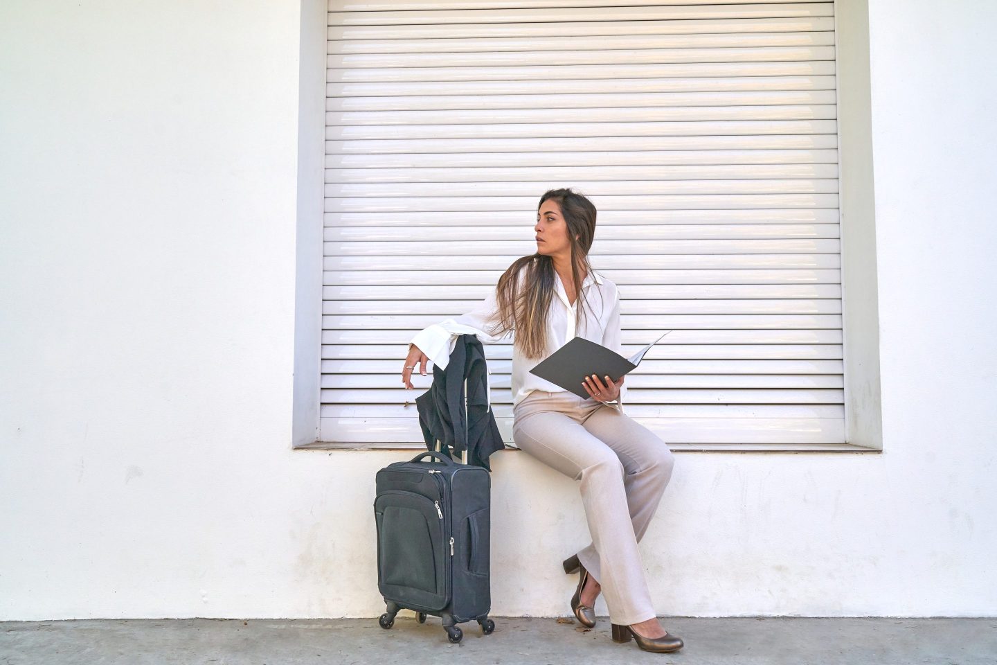 A woman sits with a suitcase and a work file on a windowsill.