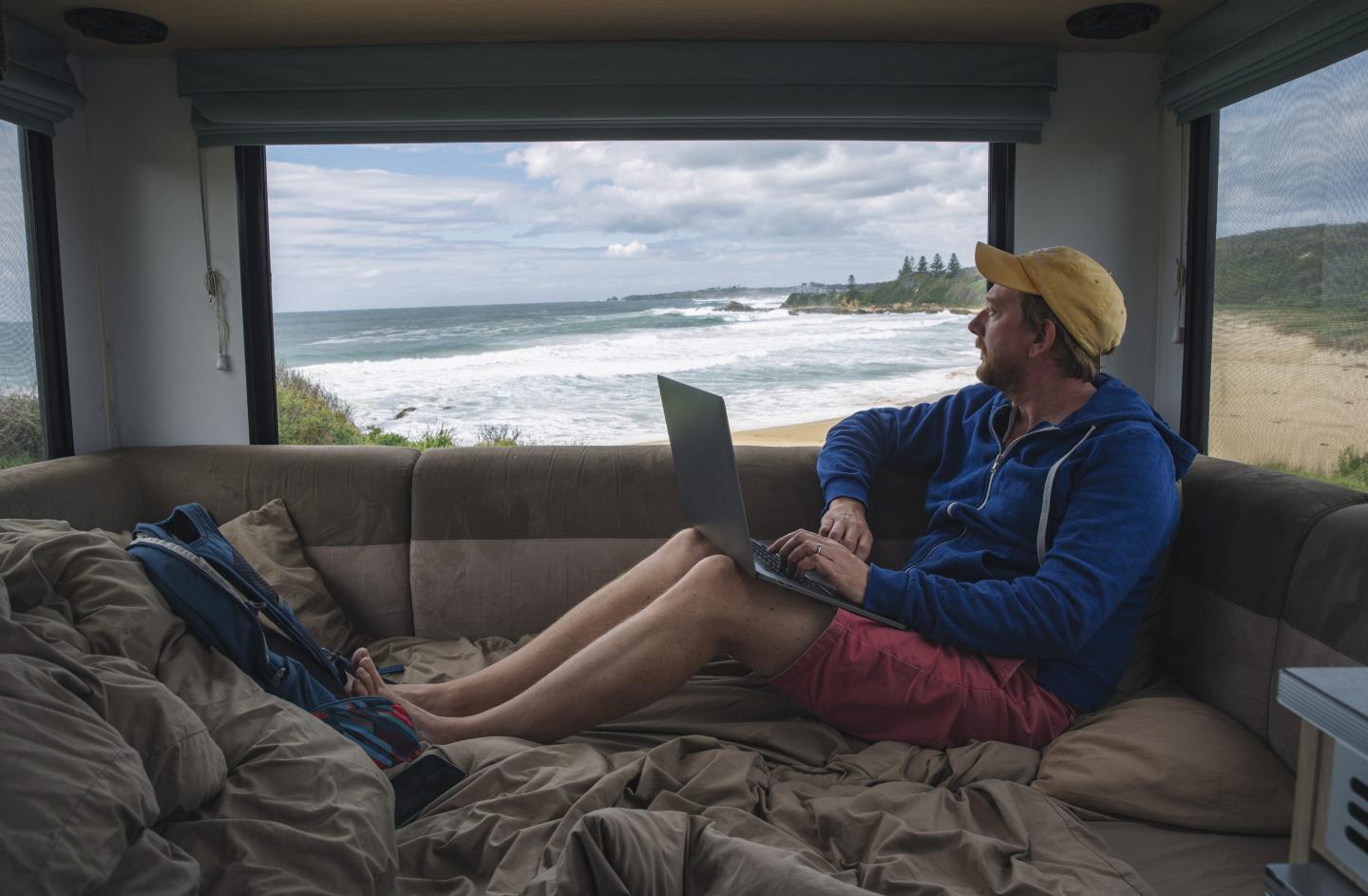 Man looking out a window while using a laptop