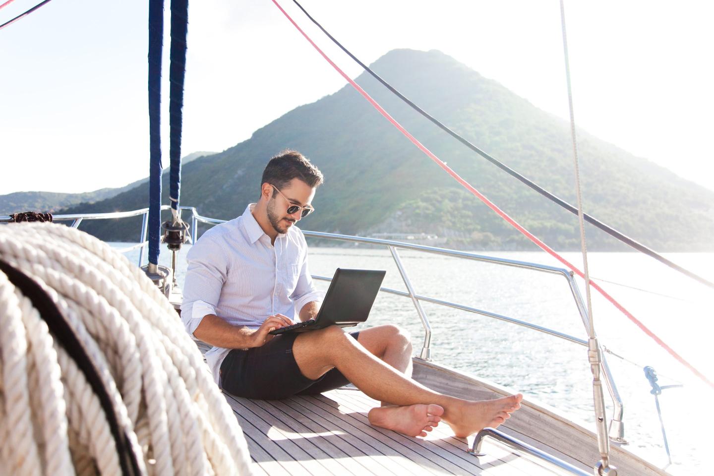 Man with laptop working on yacht deck.
