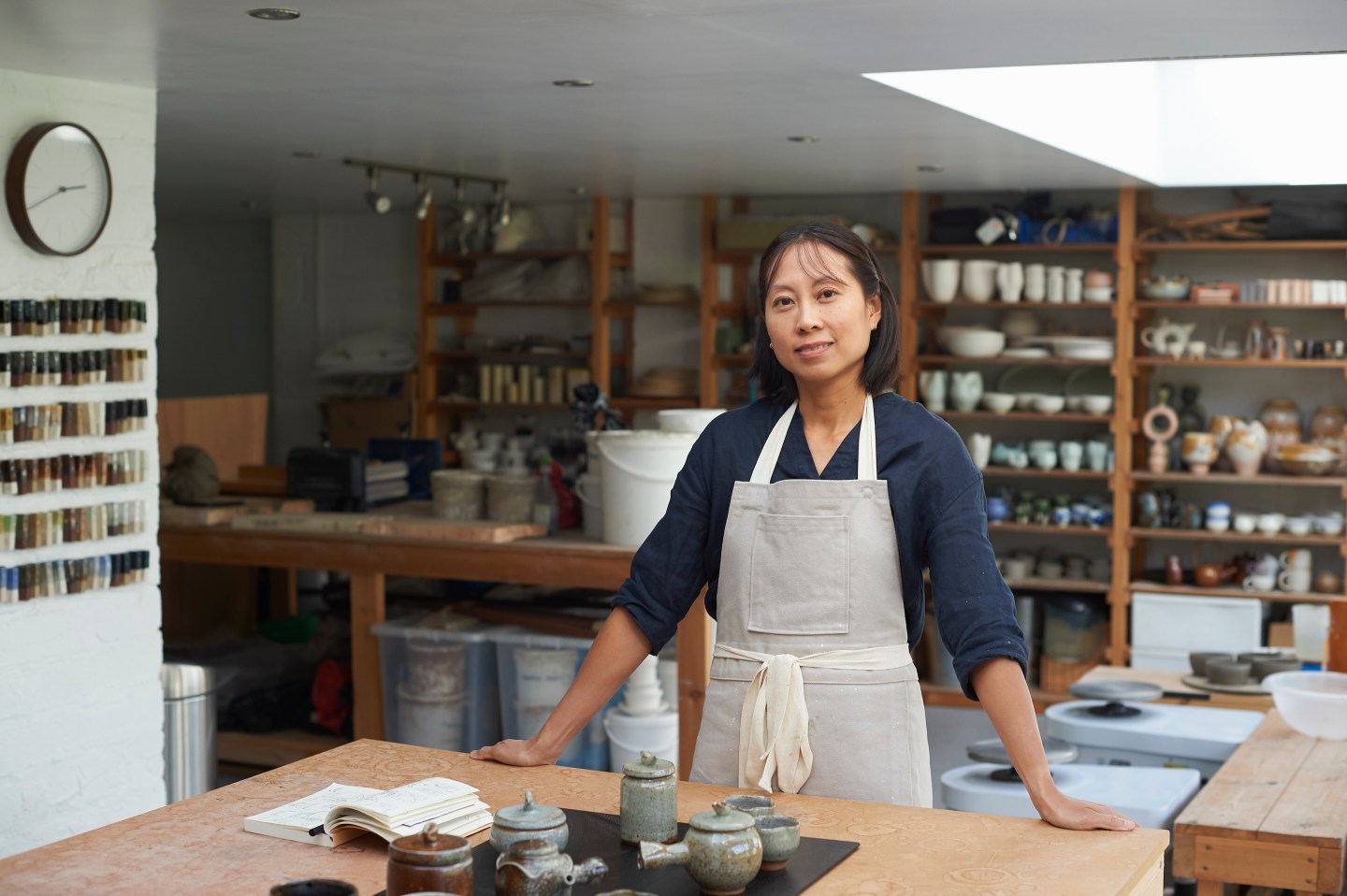 She is standing at her workbench with her sketch pad and finished ceramic items