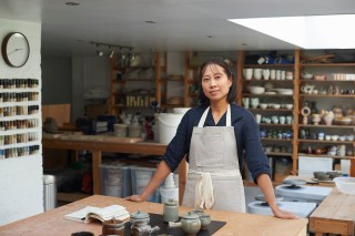 She is standing at her workbench with her sketch pad and finished ceramic items