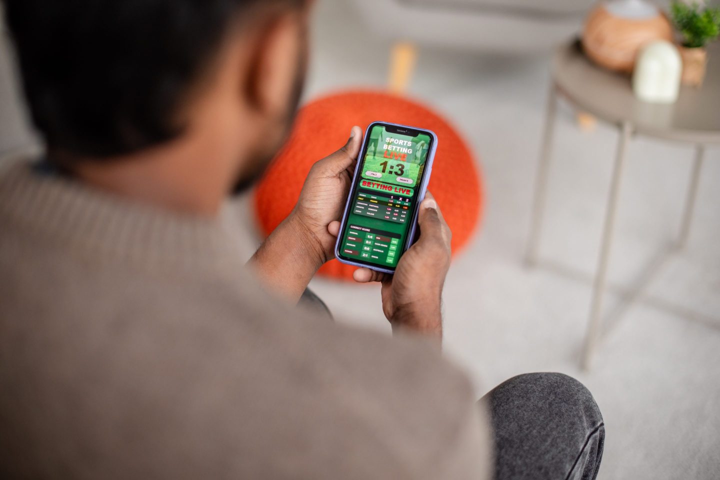 A man is engrossed in viewing the latest sports results or a mobile game on his phone screen, showcasing a modern lifestyle in a cozy home setting.