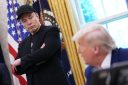 Elon Musk, standing with his arms crossed, looks down at Donald Trump sitting at his desk in the Oval Office