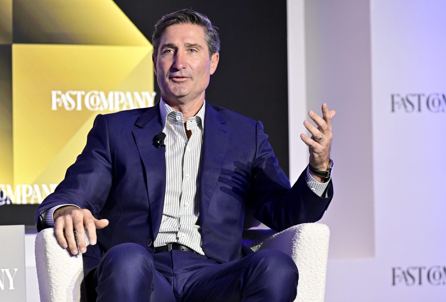 Brian Niccol sits in a white chair wearing a suit. "Fast Company" is written on the screen in the background.