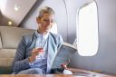 Businesswoman reading a book on private jet while drinking champagne