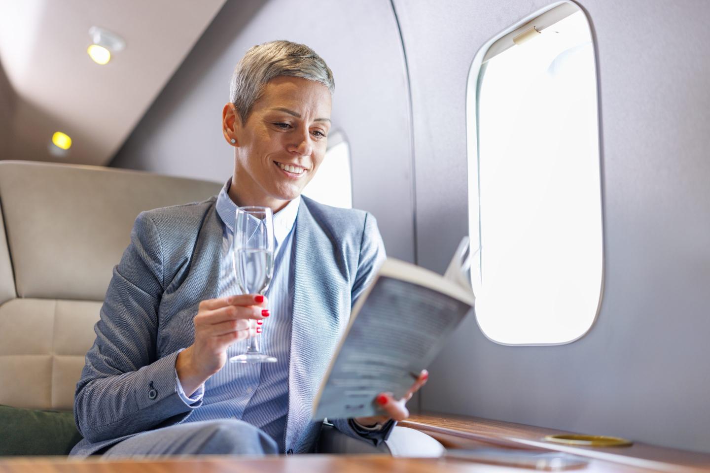 Businesswoman reading a book on private jet while drinking champagne