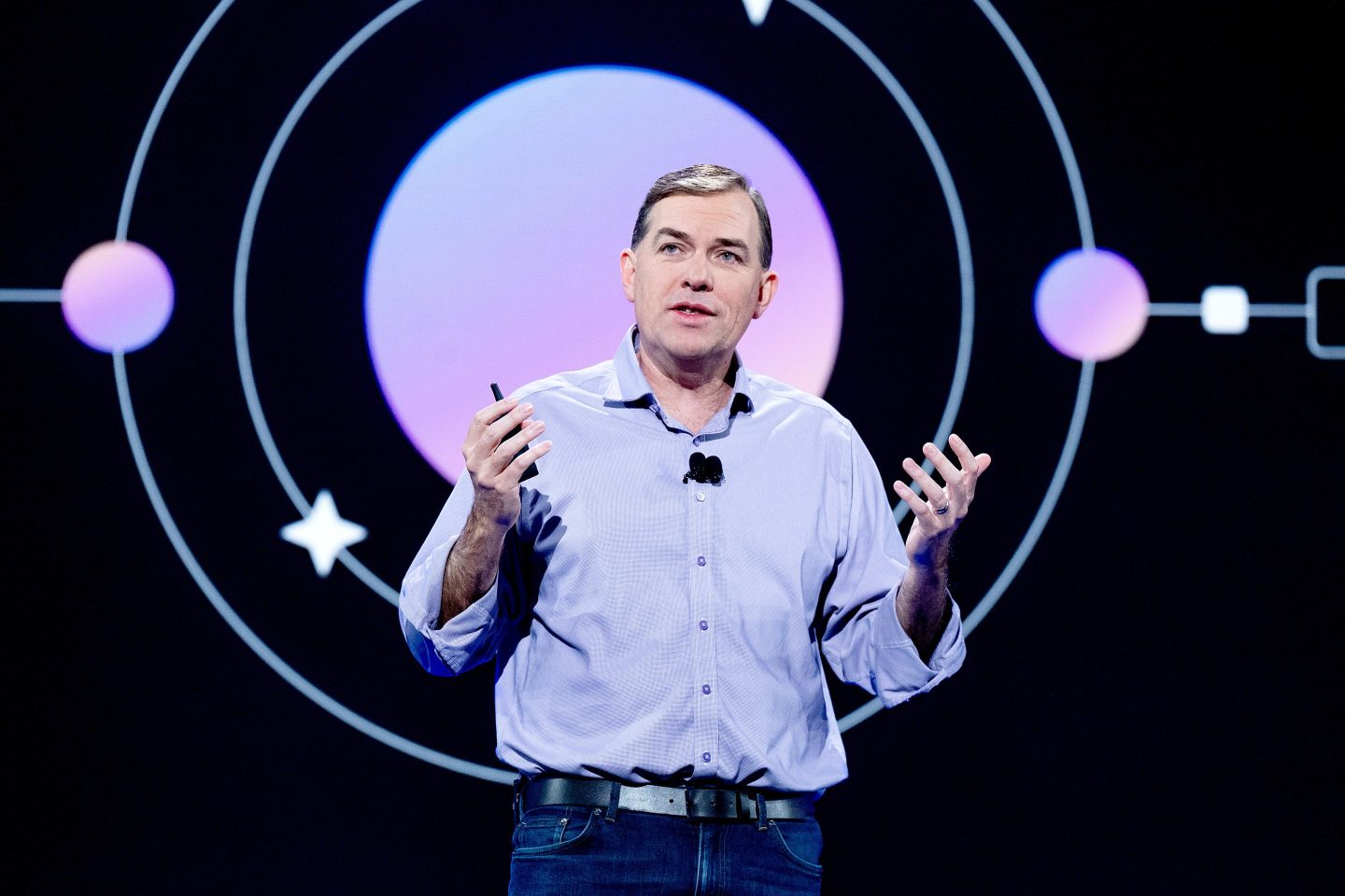 Matt Garman speaks on stage in front of a screen showing colorful concentric circles on a black background.