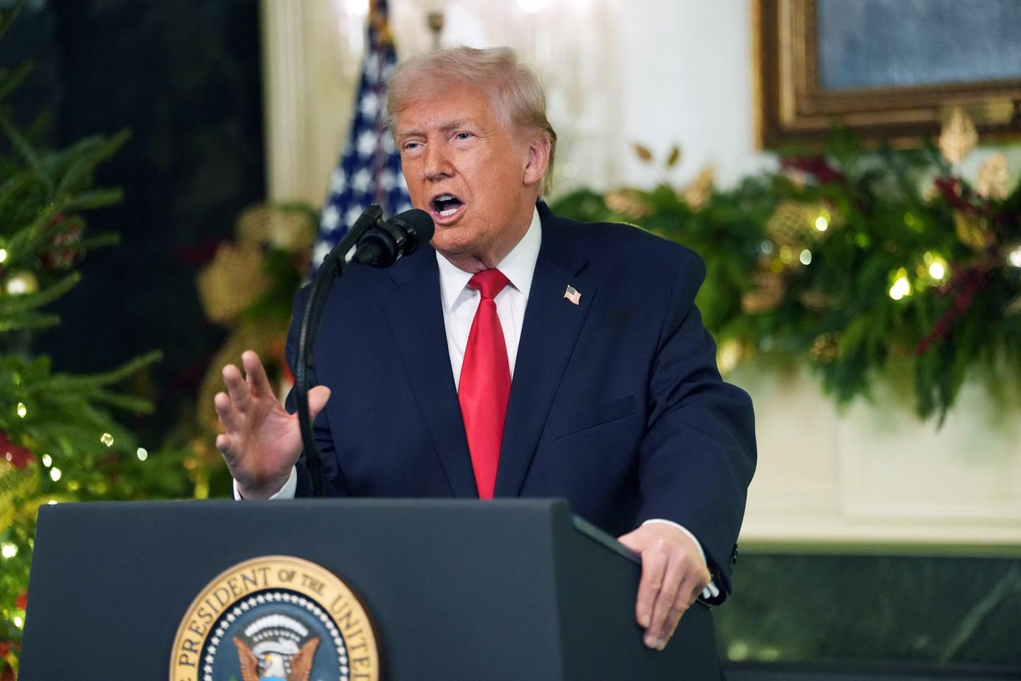 Trump stands at a podium in the Diplomatic Reception Room, which is adorned with Christmas decorations.