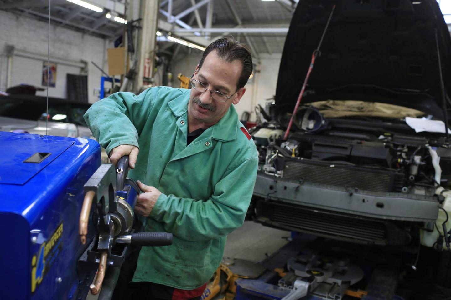 A worker in a green jacket operates a welding tool.