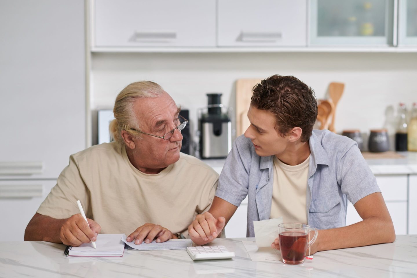 Young man helping grandfather to plan budget when they are sitting at kitchen counter
